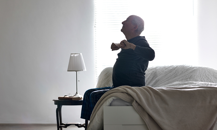 Elderly man sitting on bed and stretching arms