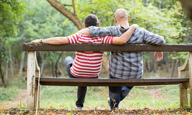 Couple sitting on bench in park facing away from camera