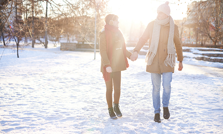 Couple walking in winter coats through a snow-covered park