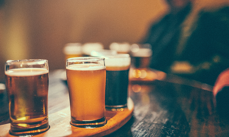 A flight of beers on a table with a person sitting behind them