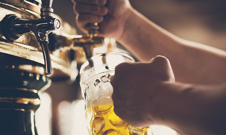 A bartender pouring light beer from a tap into a glass mug